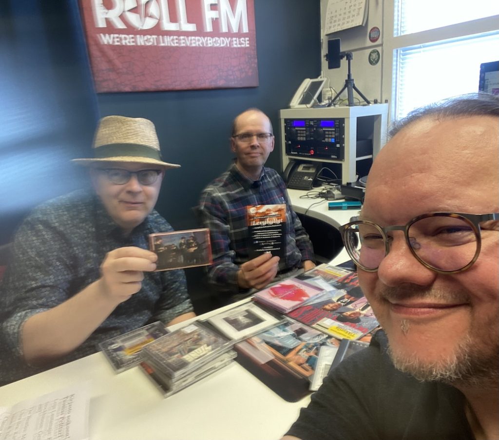 Kirjasto soikoon! -ohjelmassa Jukka Halttunen, Roll FM-kanavan Eki ja Tuomas Pelttari. Rekvisiittana Pelttarin ensimmäinen oma C-kasetti The Beatles -kokoelma Greatest, johon tehtiin kadonneen alkuperäisen tilalle uusi kuvakansi. Kuva: Tuomas Pelttari 21.5.2025