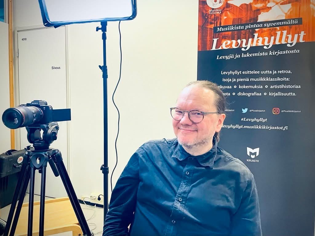 Behind The Scenes. Tuomas Pelttari Helsingin Pasilan kirjastossa musiikkiosastolla 11.12.2024 Levyhyllyt 10 vuotta -videon kuvaustauolla. Kuva: Riitta Taarasti