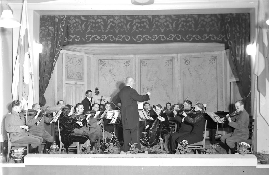 Jousin, puhaltimin ja yhdellä kosketinsoittajalla varustettu parikymmenpäinen sinfonietta pitää kapellimestari Kiltilän johtamana juhlakonserttia Suojeluskuntatalossa (nykyinen Sininen Talo) 1940-luvulla.
Sotilasviulistit lienevät rintamalta lomalla. Kyseessä on vuonna 1923 perustettu Salon Amatööriorkesteri.
Sellisti on rouva Lumilla Vilhonen. Kuva: Salo-Uskelan seuran arkisto